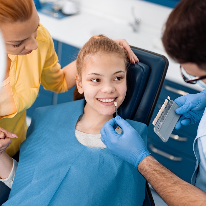 girl in dentist's chair with mother and dentist standing on either side