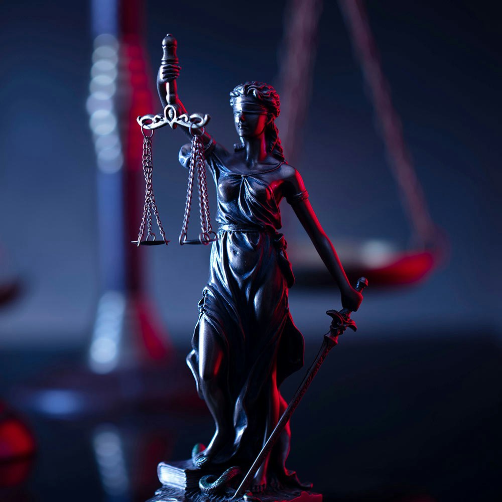 Close up of Lady Liberty statue in a dark room with red and blue lights and justice scales and gavel in the background