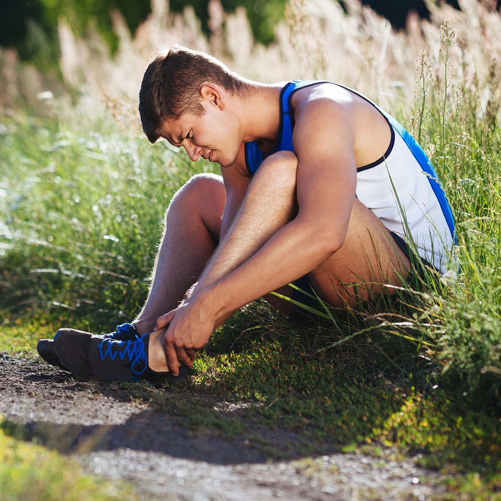 Young man holding ankle in pain after running