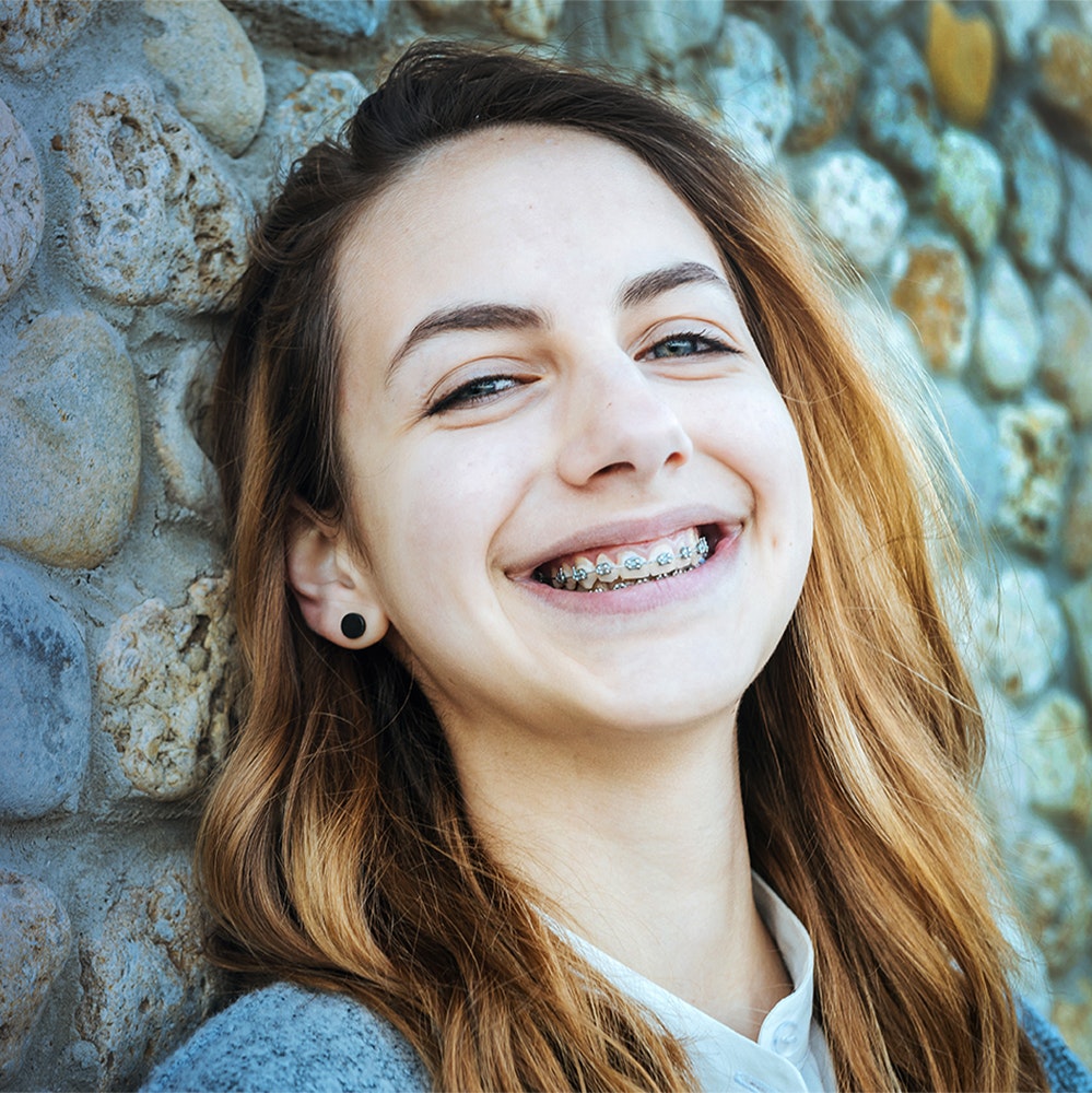 young girl leaning up against a wall smiling with braces