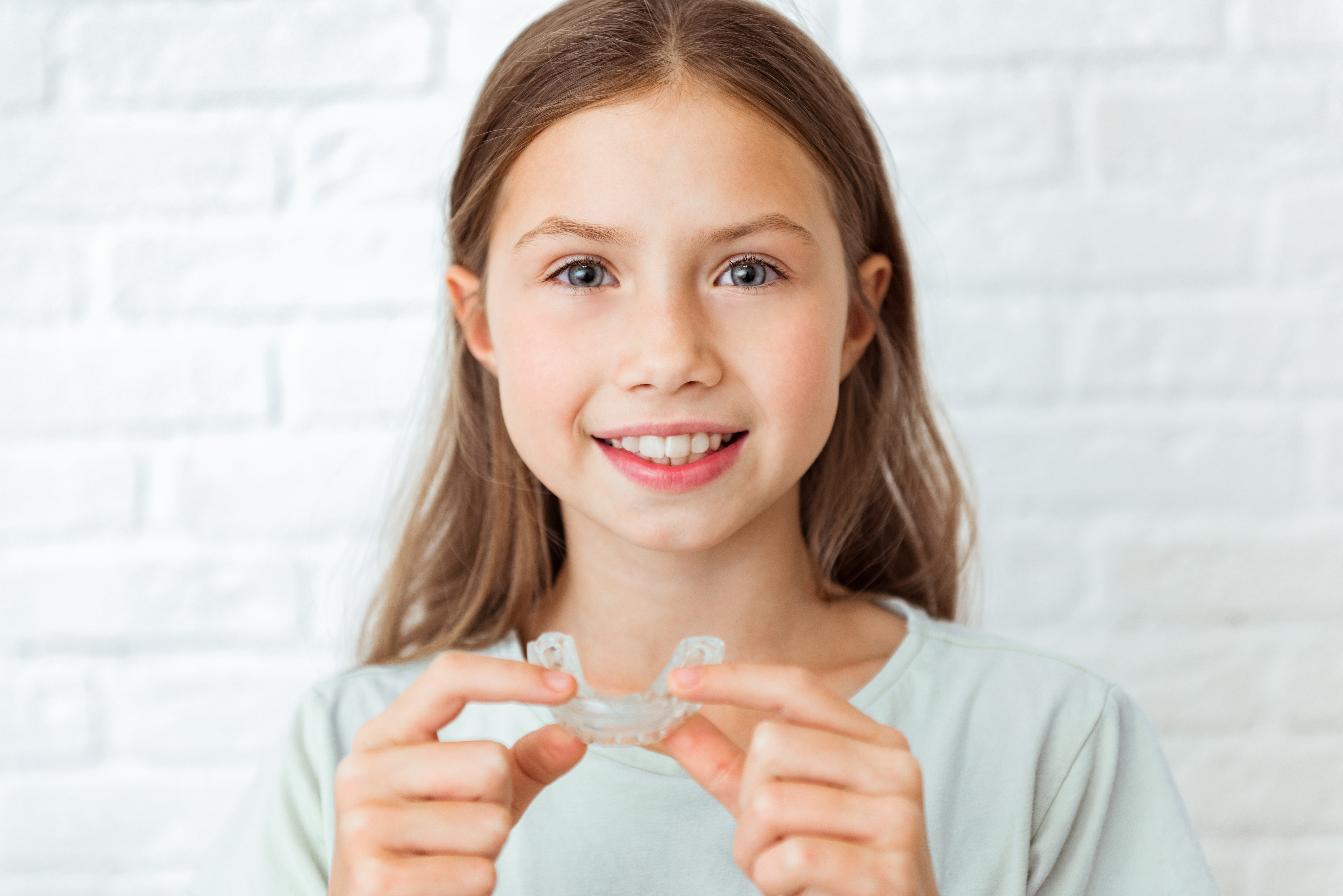 Young girl smiling while holding Invisalign aligners