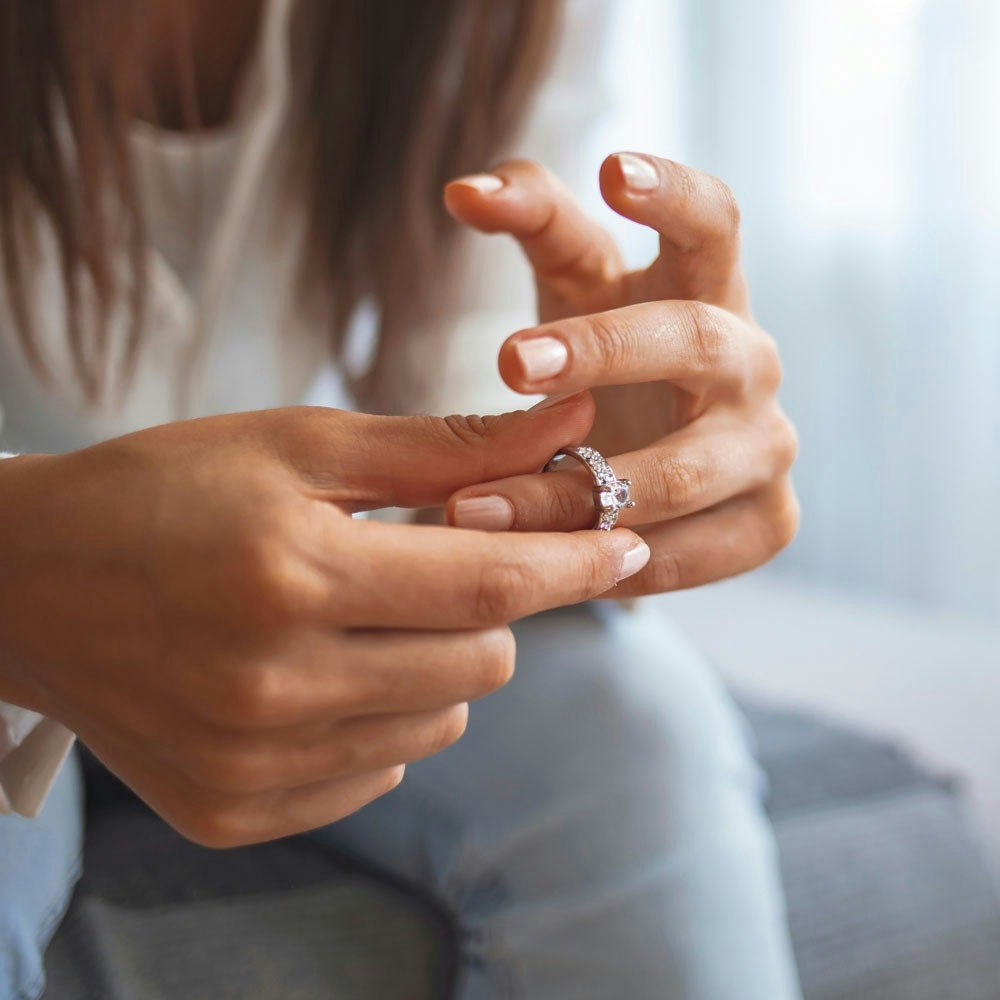 Woman taking off wedding ring as she considers divorce