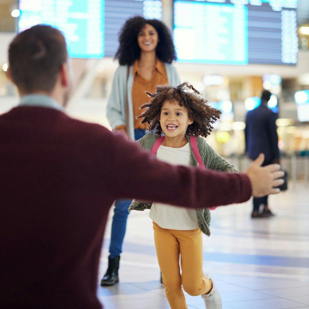 Excited girl at airport running from mother to father