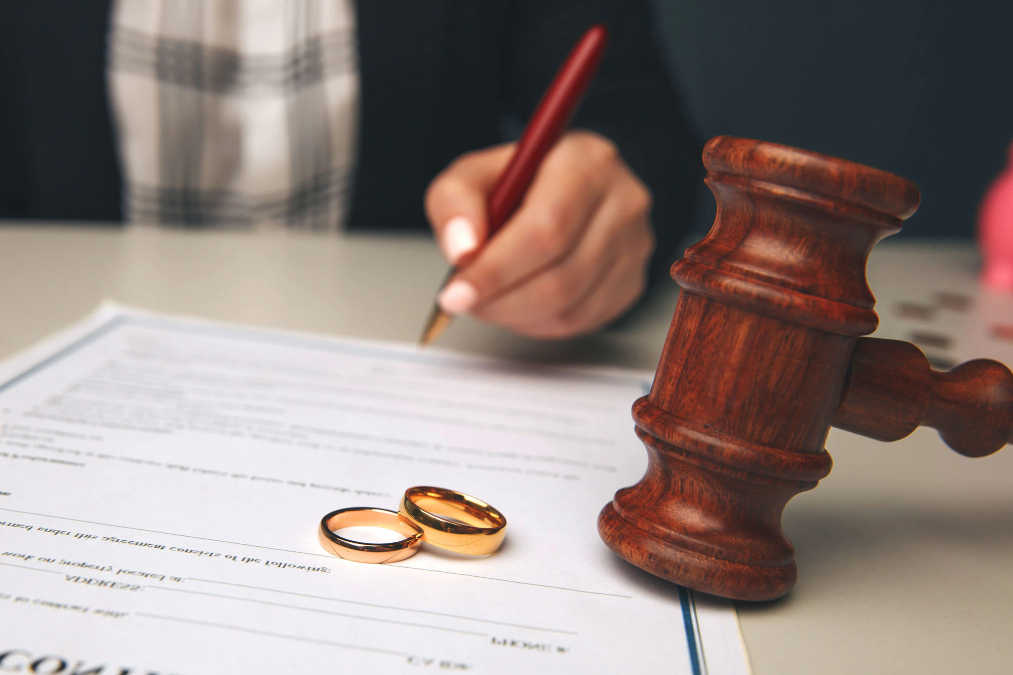 a hand signing a document with a gavel and wedding bands in the foreground