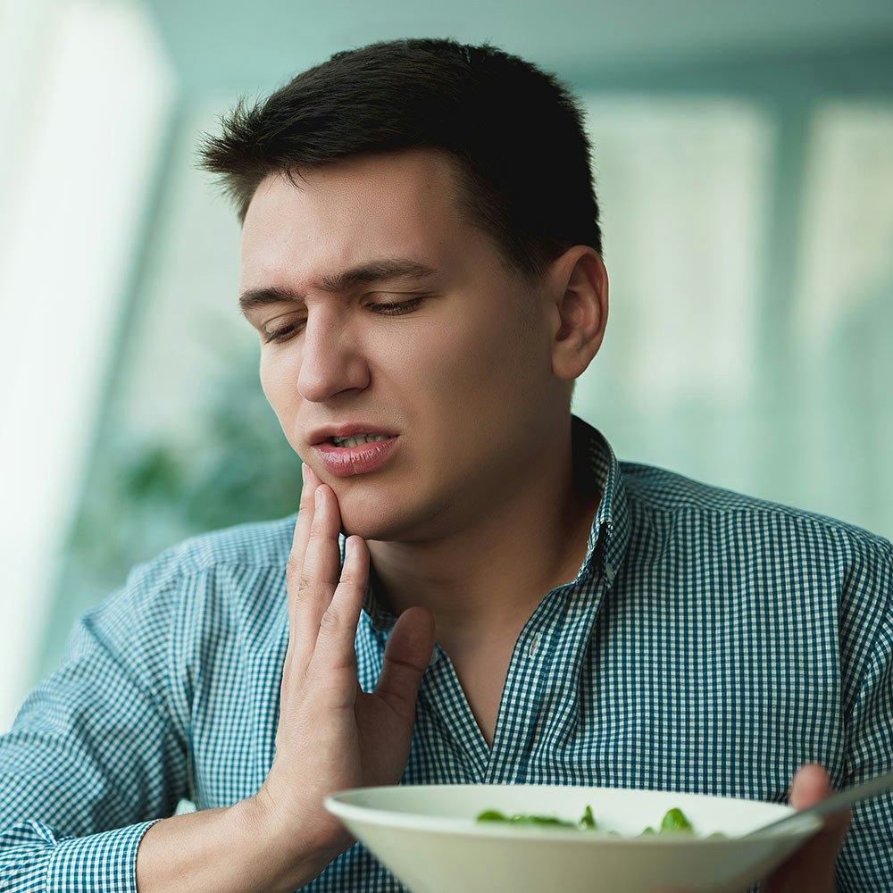 Man gripping mouth in pain while eating