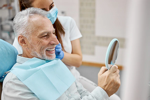 Man at the dentist smiling in a hand mirror