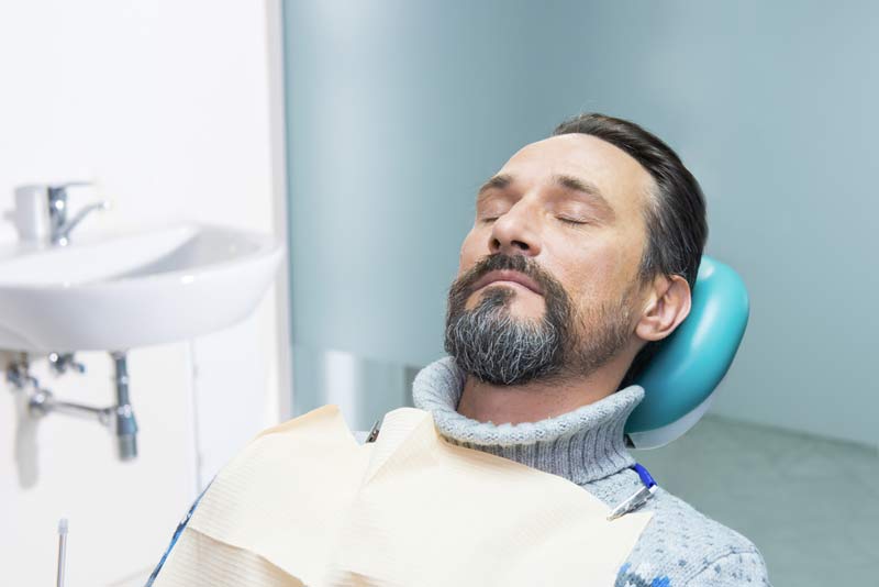 Man resting with eyes closed in dental chair wearing protective bib during appointment
