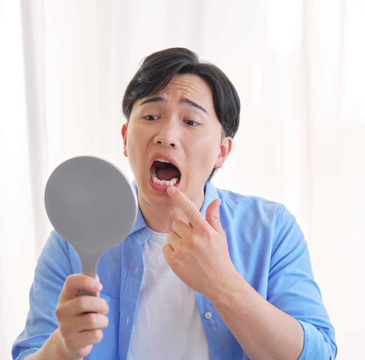 Man holding handheld mirror and pointing to lower tooth with concerned expression