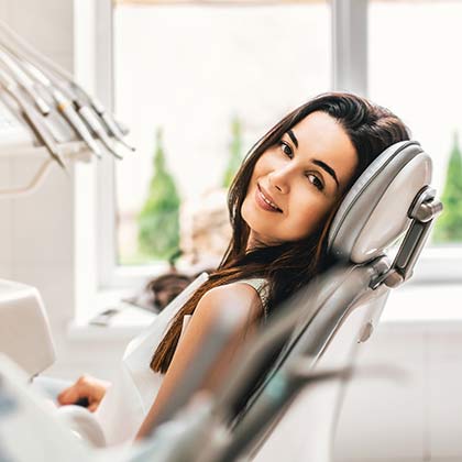 Smiling woman with dark hair leaning back comfortably in a dental chair