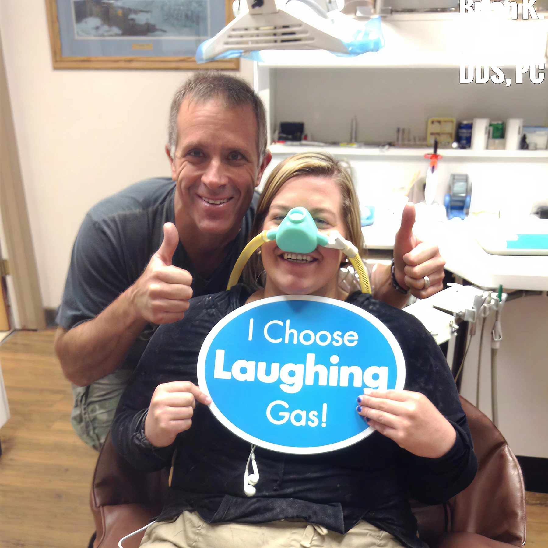 Dr. Tavoian giving a thumbs up next to a patient wearing a nitrous oxide mask and holding an "I Choose Laughing Gas" sign