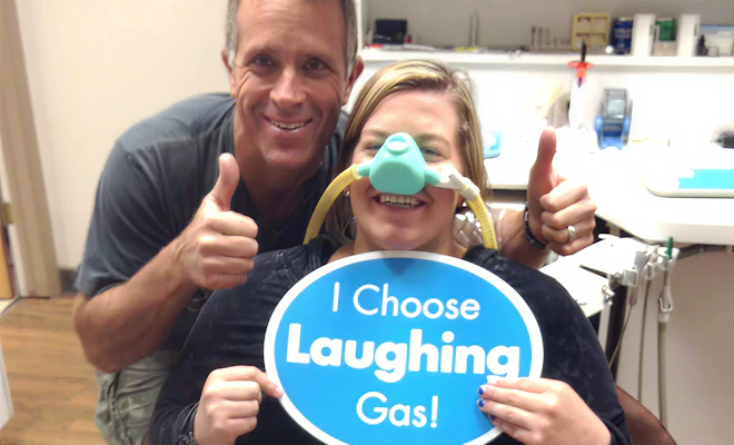 Dr. Tavoian giving a thumbs up next to a patient wearing a nitrous oxide mask and holding an "I Choose Laughing Gas" sign