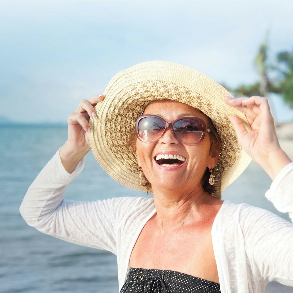 Middle aged woman on the beach smiling after crown lengthening treatment