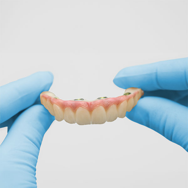gloved hands holding implant-supported dentures
