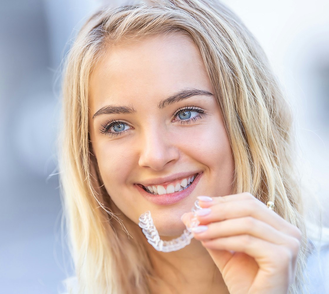 Smiling woman holding clear aligner