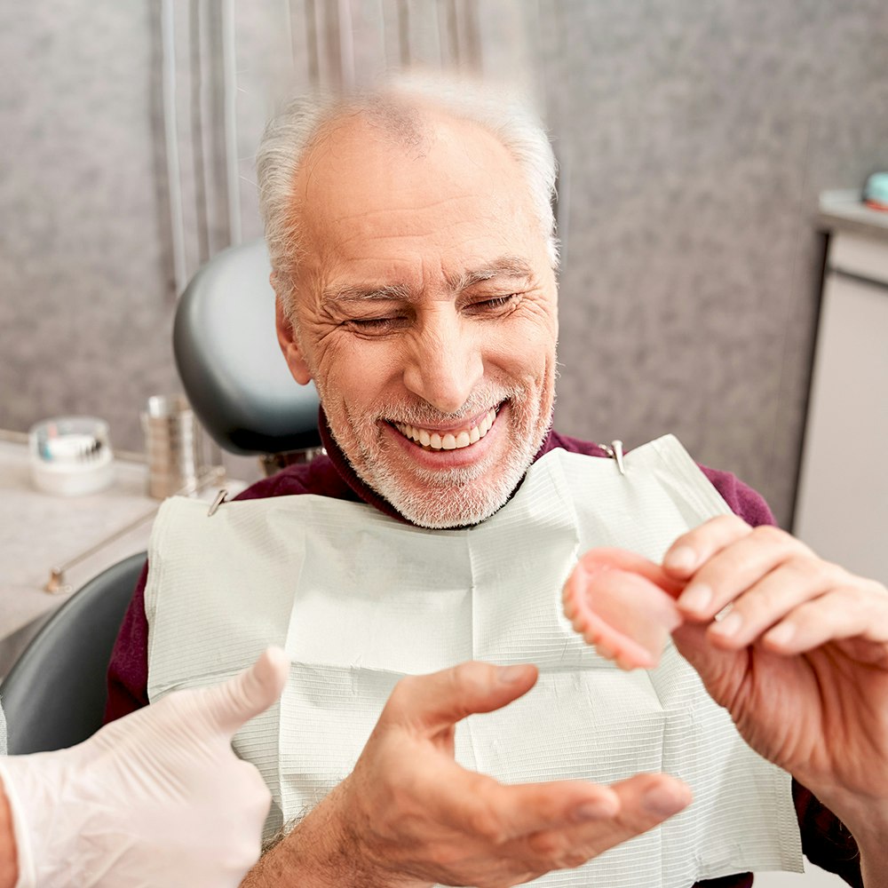 Smiling older patient putting in a traditional denture