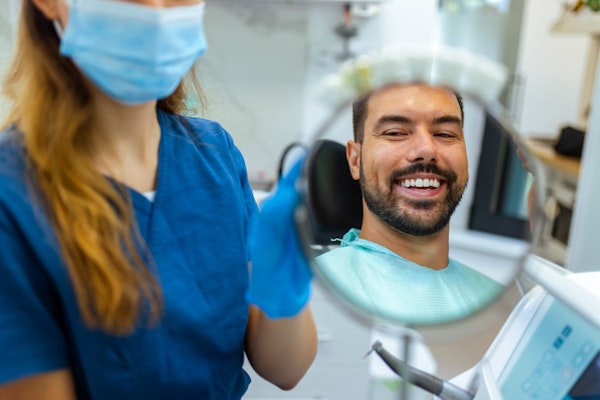 Man smiling in the mirror at the dentist