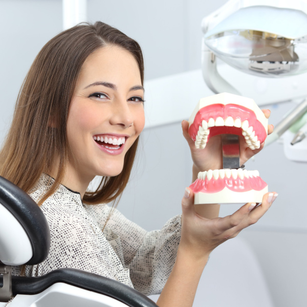 smiling woman holding a model of teeth