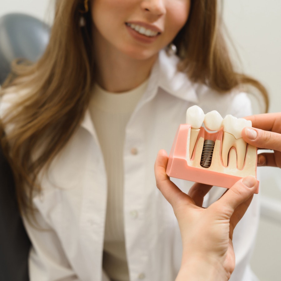 dentist showing woman a model of a jaw with dental implants
