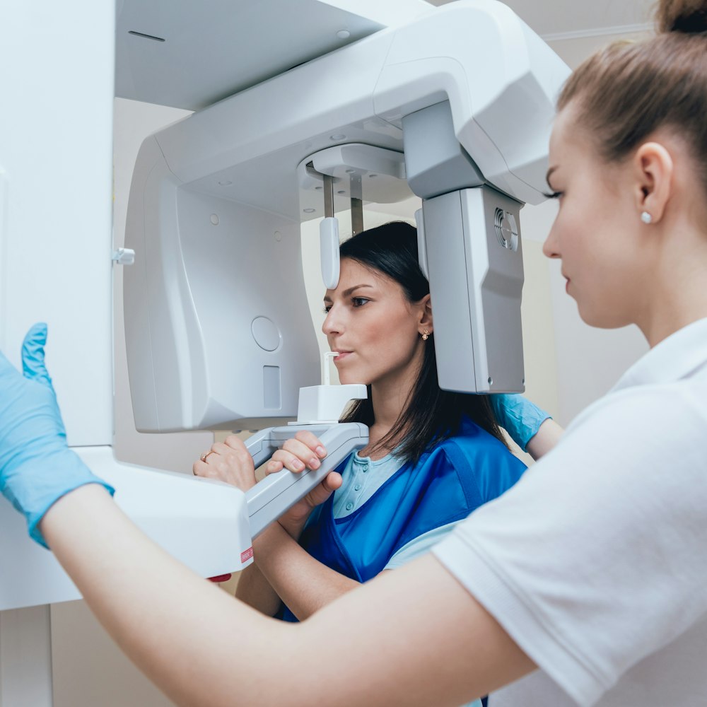 Patient undergoing 3D cone beam scan with dental assistant operating imaging machine