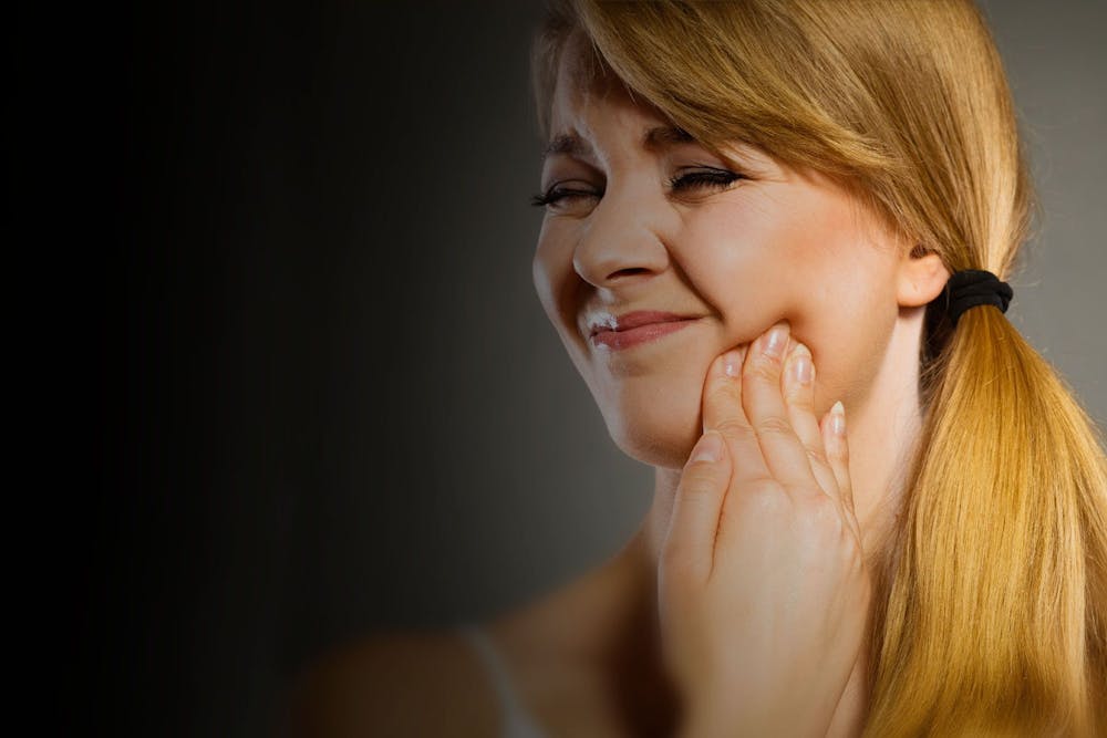 Blonde woman with hand on jaw in pain