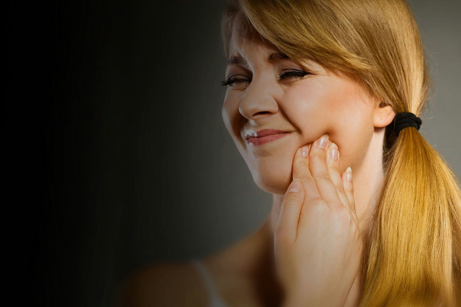 Blonde woman with hand on jaw in pain