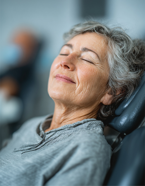 Older woman relaxing in a dental chair with eyes closed and a peaceful expression.