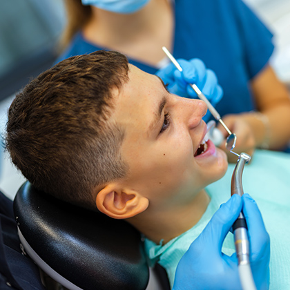 Boy receiving dental care while seated in a treatment chair, smiling during the procedure.