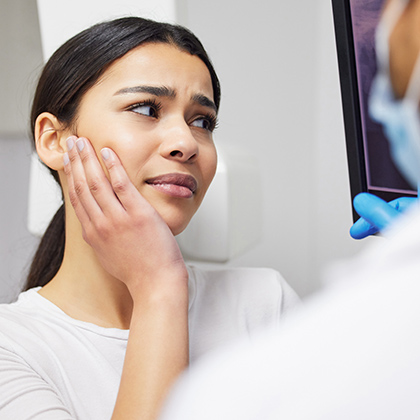 Concerned woman touching her cheek while discussing jaw pain with a dentist.