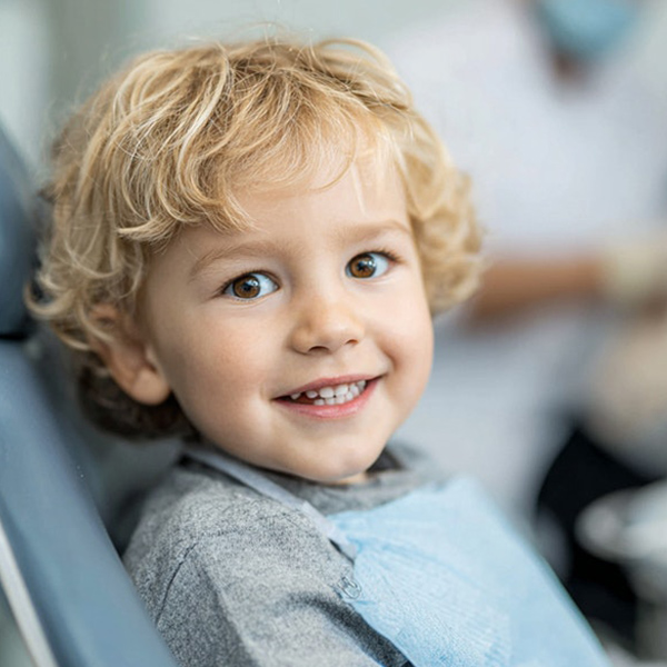 Young child smiling while seated in a dental chair, wearing a disposable bib.