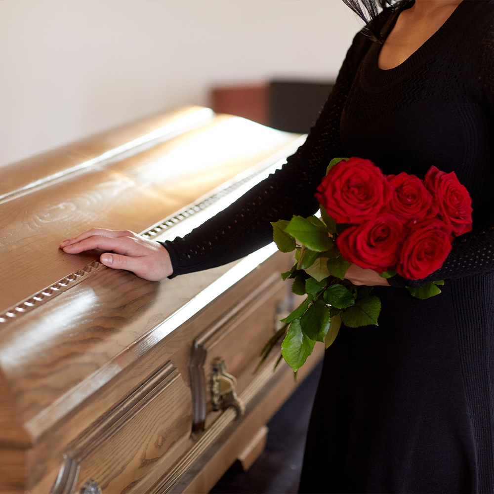 a woman touching a casket, holding roses