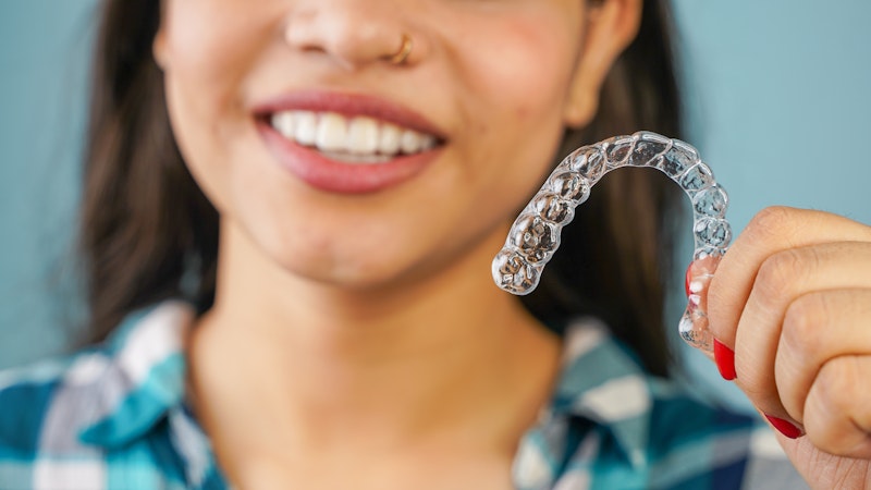 Smiling woman holding an Invisalign aligner
