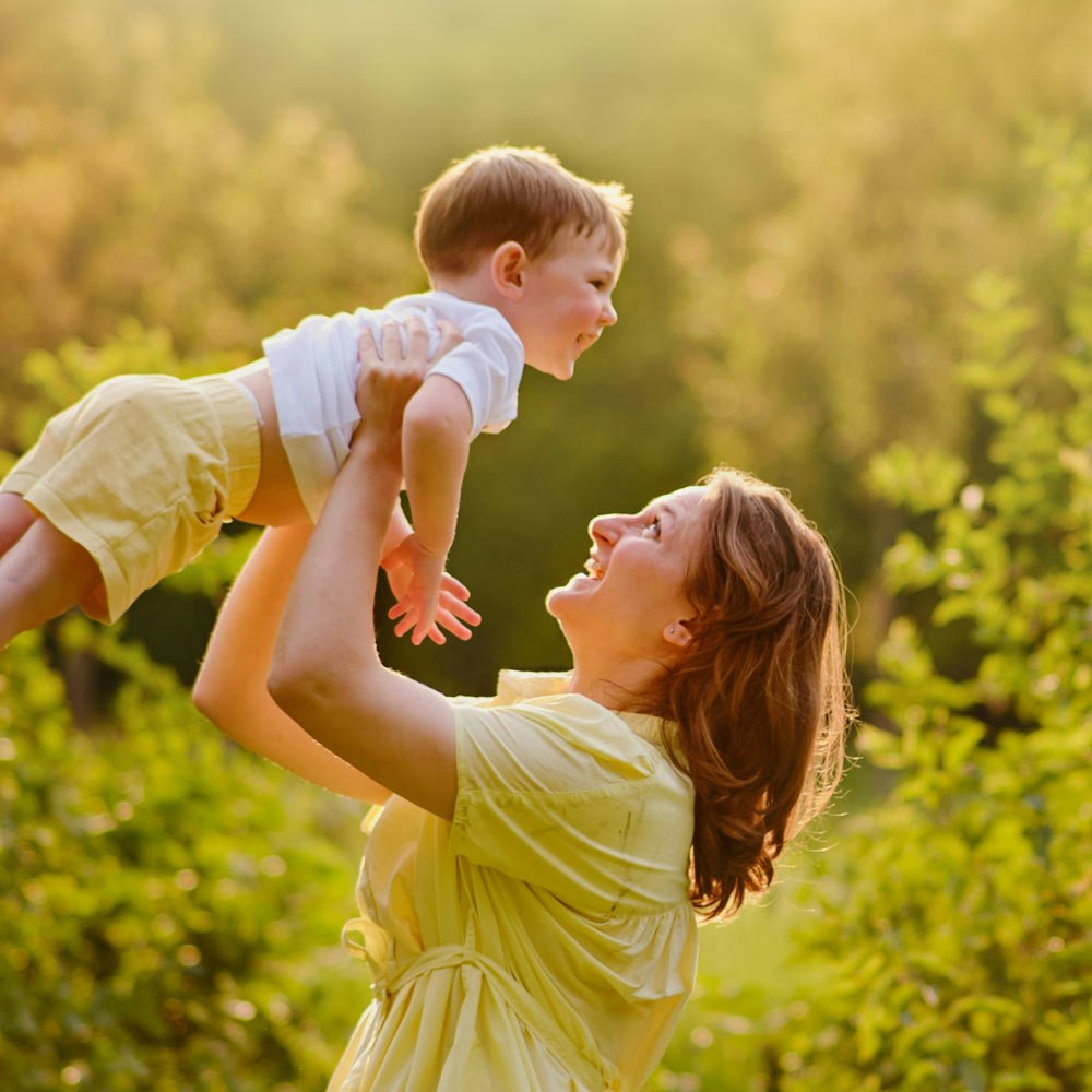 Young mother lifting up her son in her arms outdoors