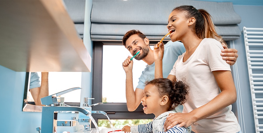Couple with young girl brushing teeth together and looking in the mirror