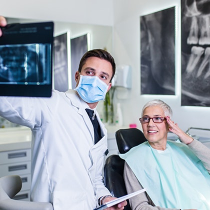 Masked dentist showing woman an image on a monitor