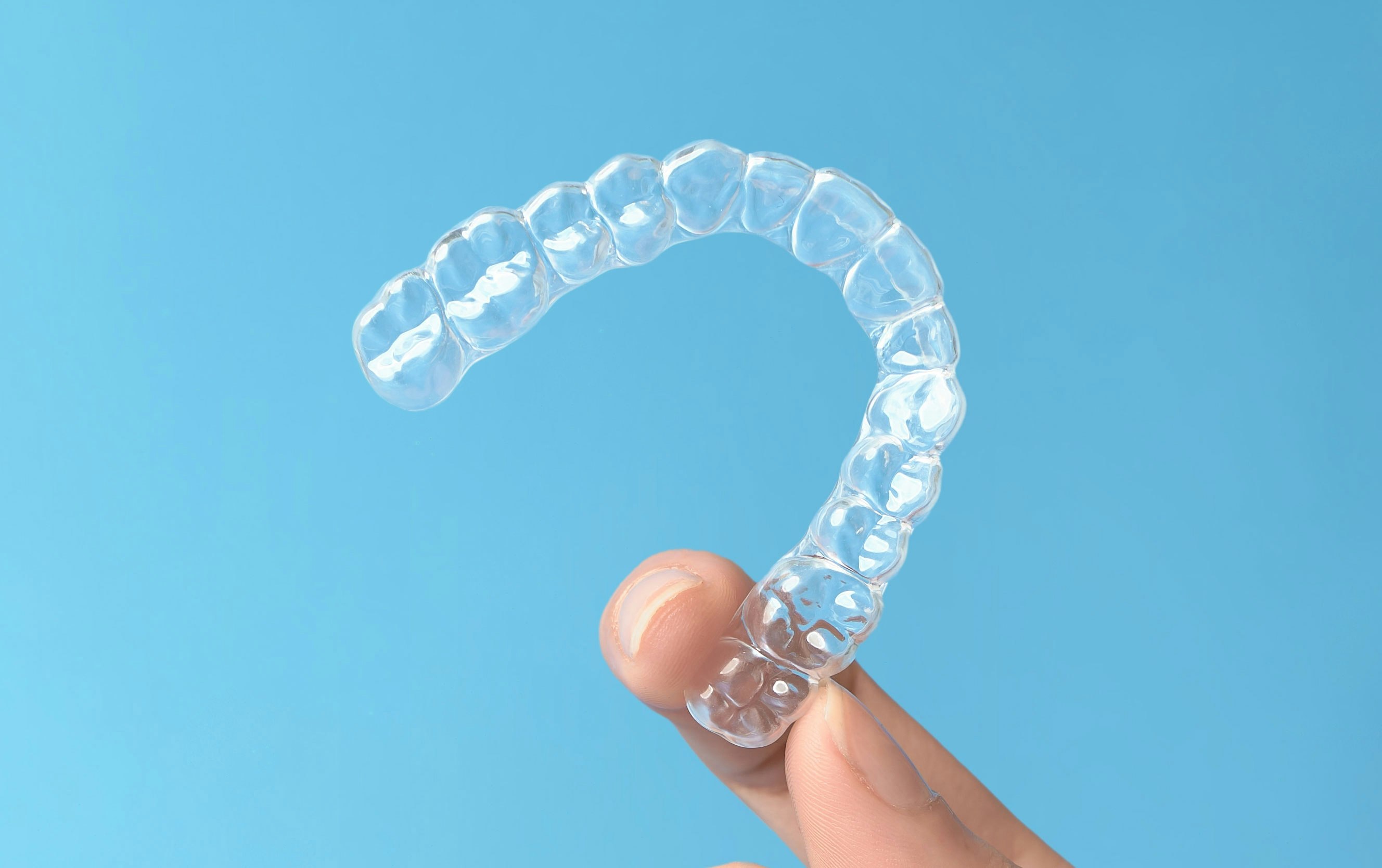 Hand holding a clear Invisalign aligner against a blue background