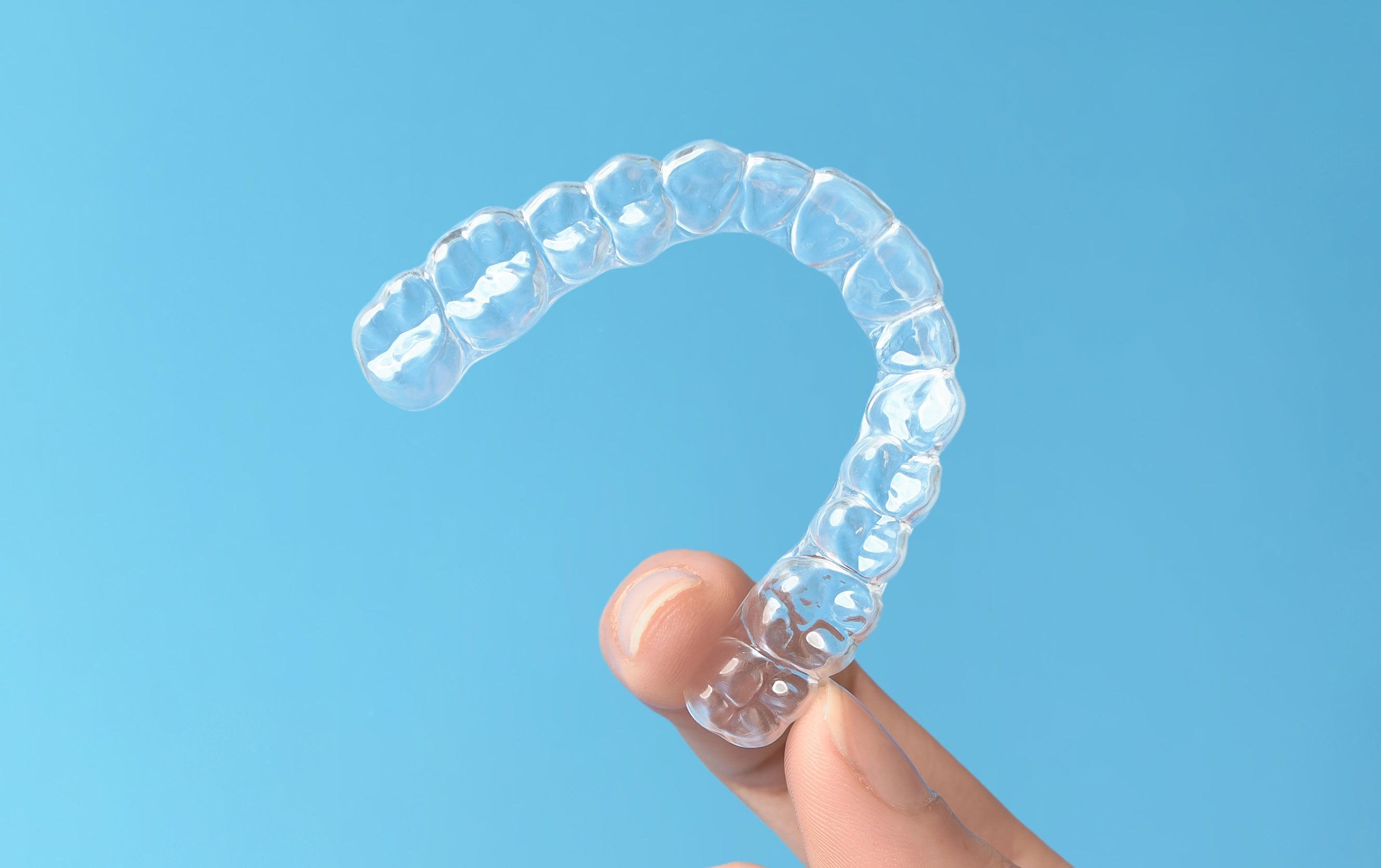Hand holding a clear Invisalign aligner against a blue background