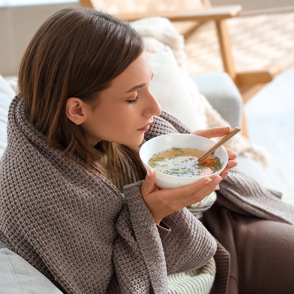 A woman eating soup with a blanket on the couch after implant surgery