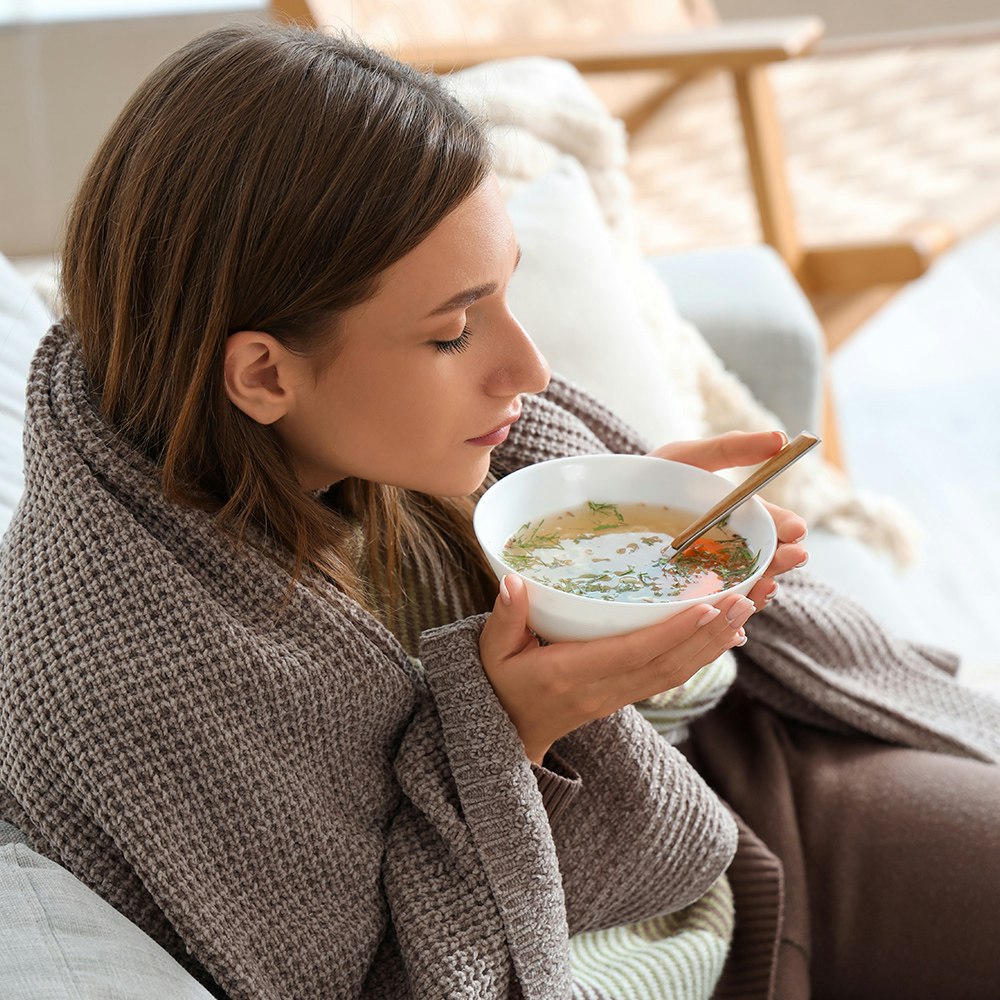 A woman eating soup with a blanket on the couch after implant surgery