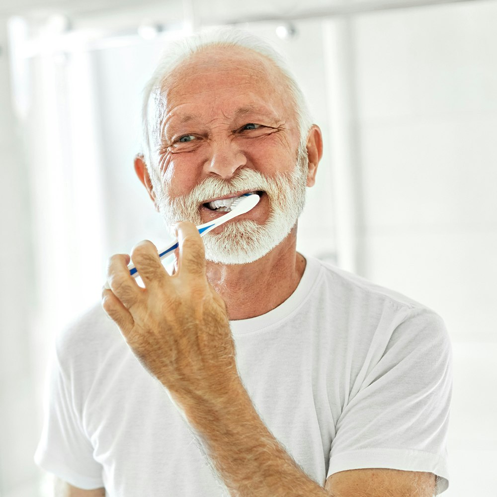 A mature man brushing his teeth in the mirror