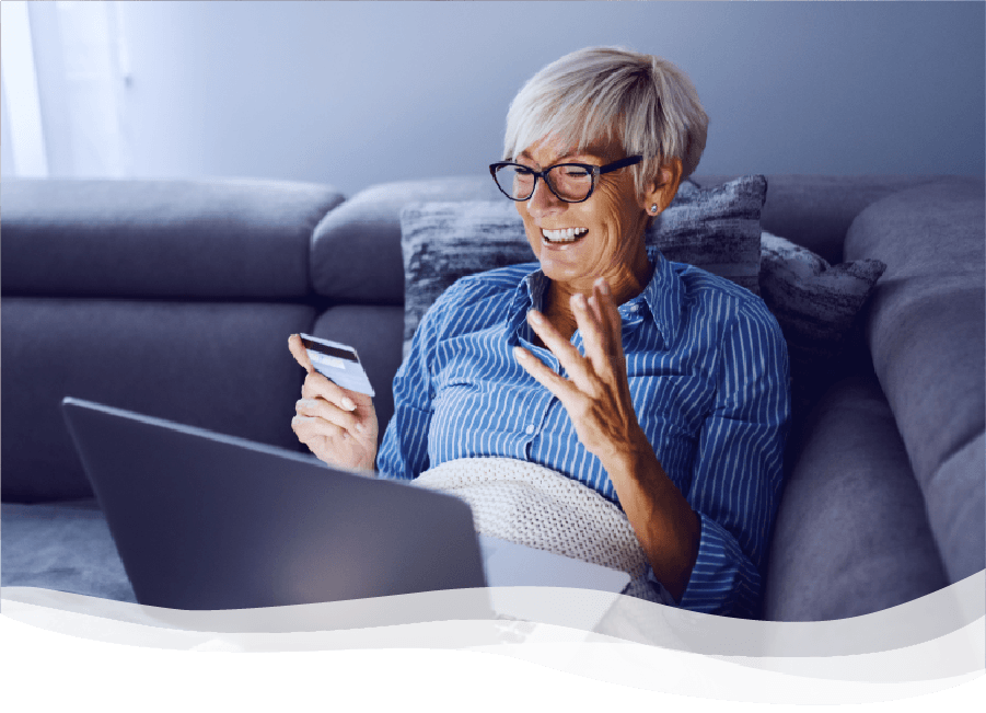 Mature woman smiling and holding credit card while looking at laptop on couch