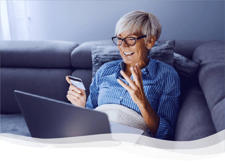 Mature woman smiling and holding credit card while looking at laptop on couch