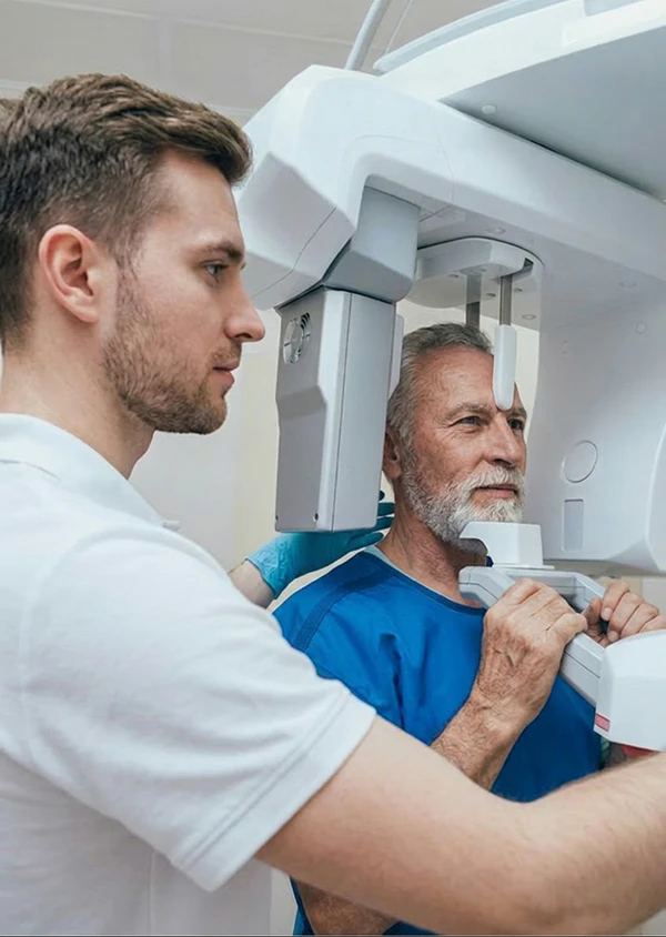 Dental technician positioning an older male patient in a panoramic X-ray machine