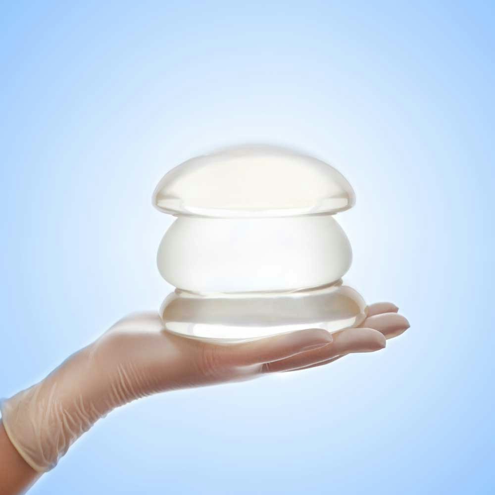 hand holding breast implants stacked on top of each other