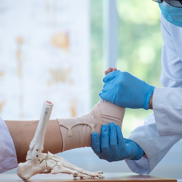 Doctor examining someone's wrapped foot after surgery with a skeletal model of a foot and ankle near by