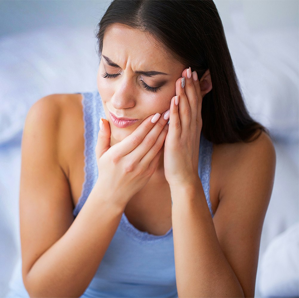 Young woman massaging her jaw in pain and considering BOTOX for TMJ