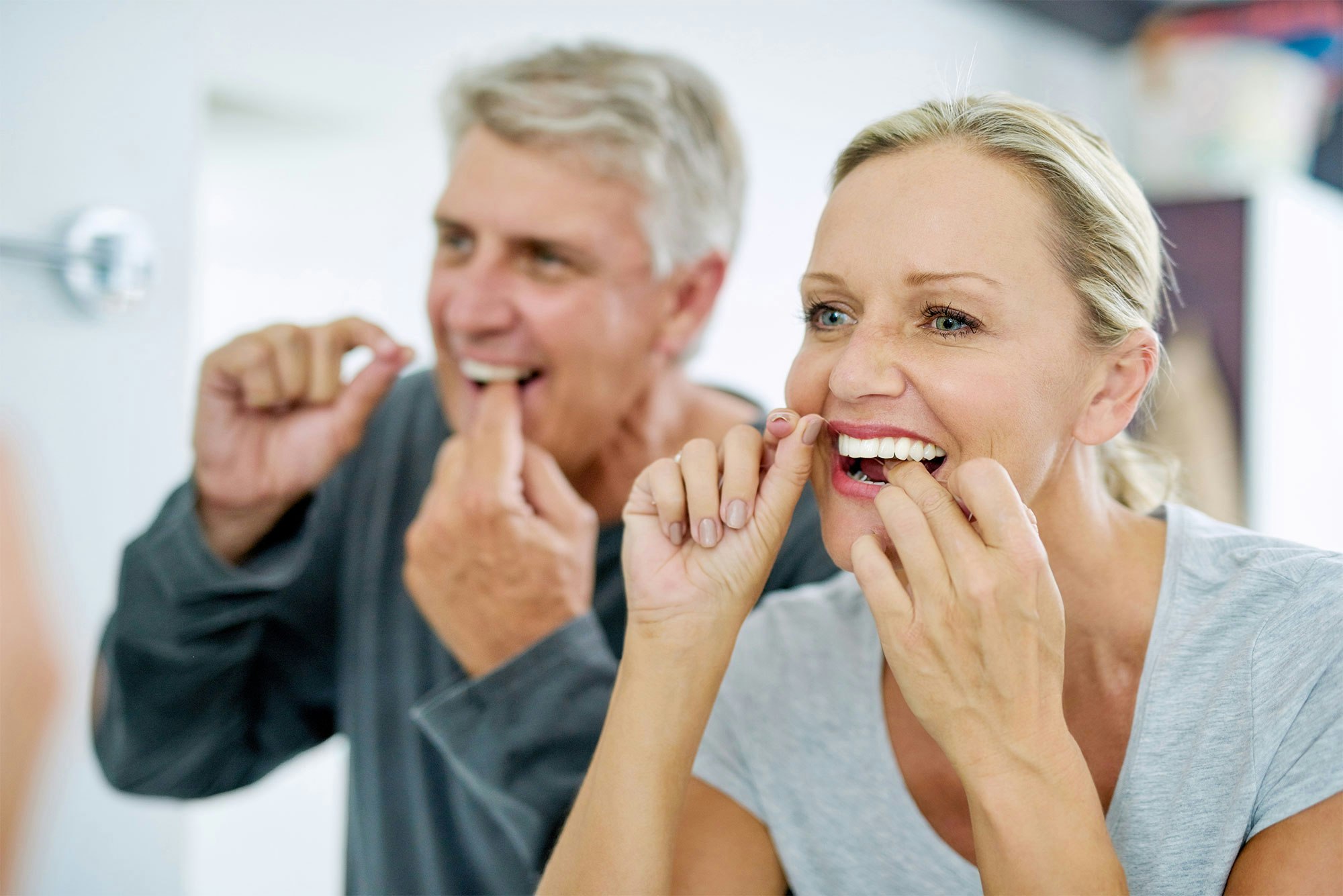 couple with implant dentures flossing their teeth