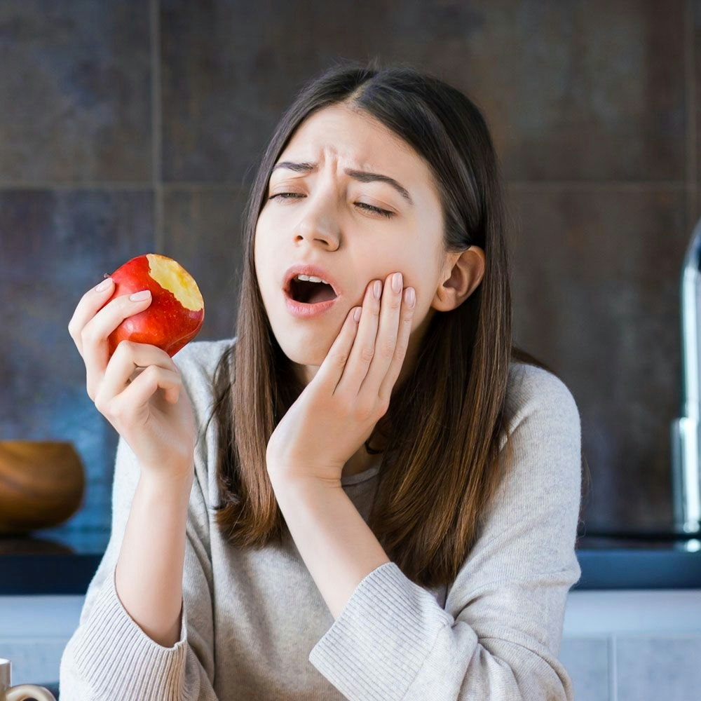 Young woman holding jaw in pain after eating an apple