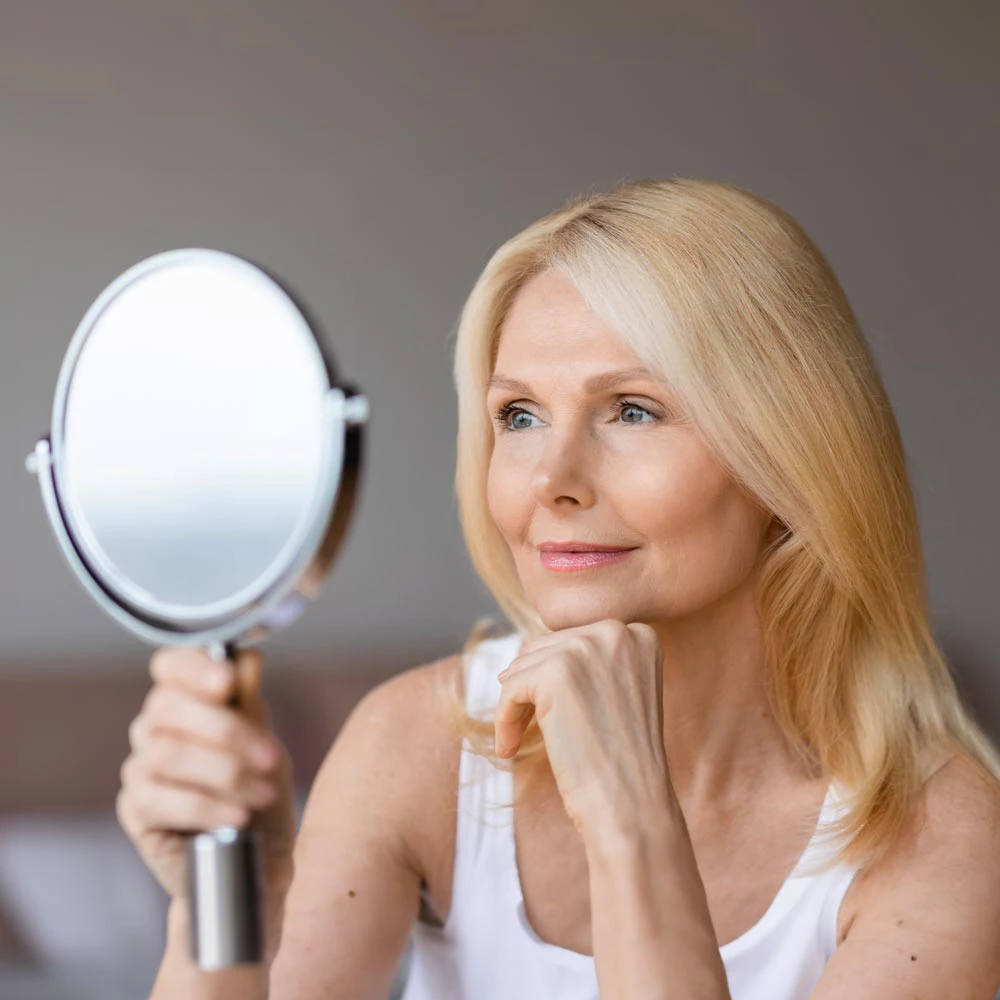 Smiling middle-aged woman looking into mirror