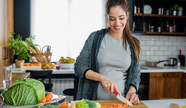 Smiling pregnant woman chopping vegetables
