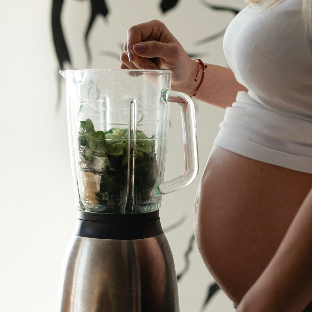 Side profile of pregnant woman putting vegetables in the blender